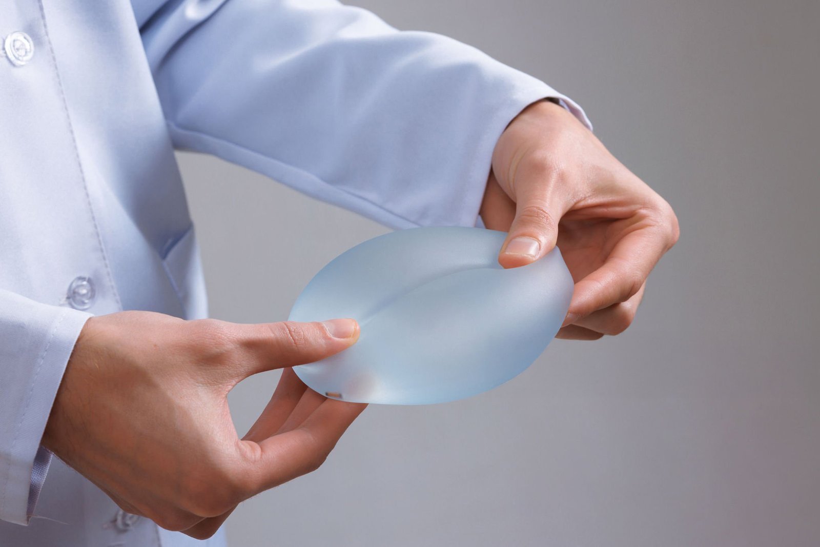 Surgeon compresses silicone breast implant for mammoplasty breast augmentation and cosmetic shape correction